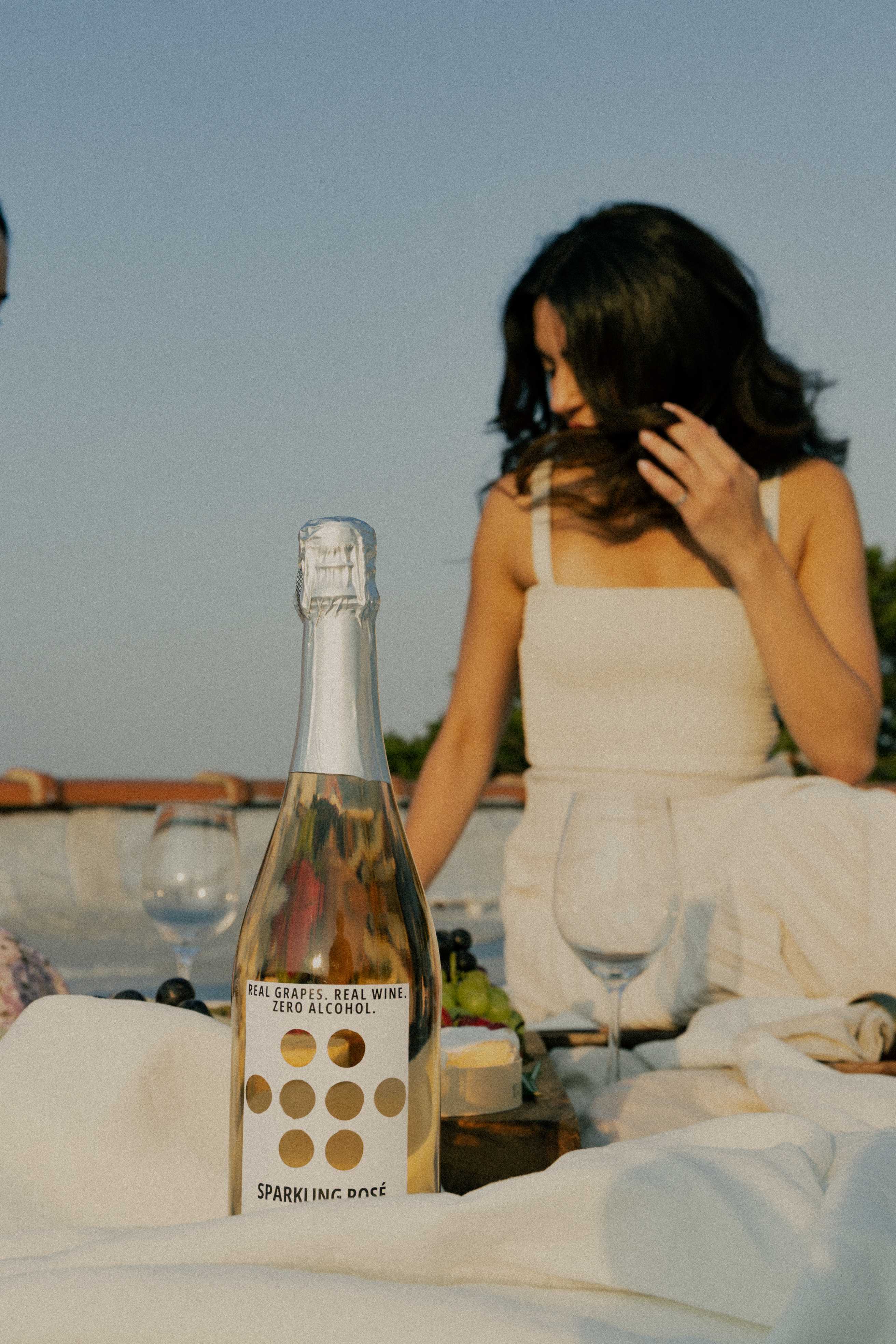 bottle-of-le-tour-non-alcoholic-sparkling-wine-on-picnic-blanket-with-blurred-person-in-background